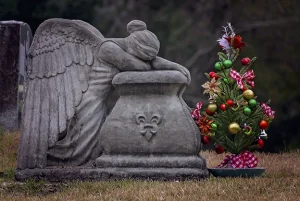 Stone angel statue resting its head on folded arms beside a decorated Christmas tree, symbolizing grief and remembrance during the holidays